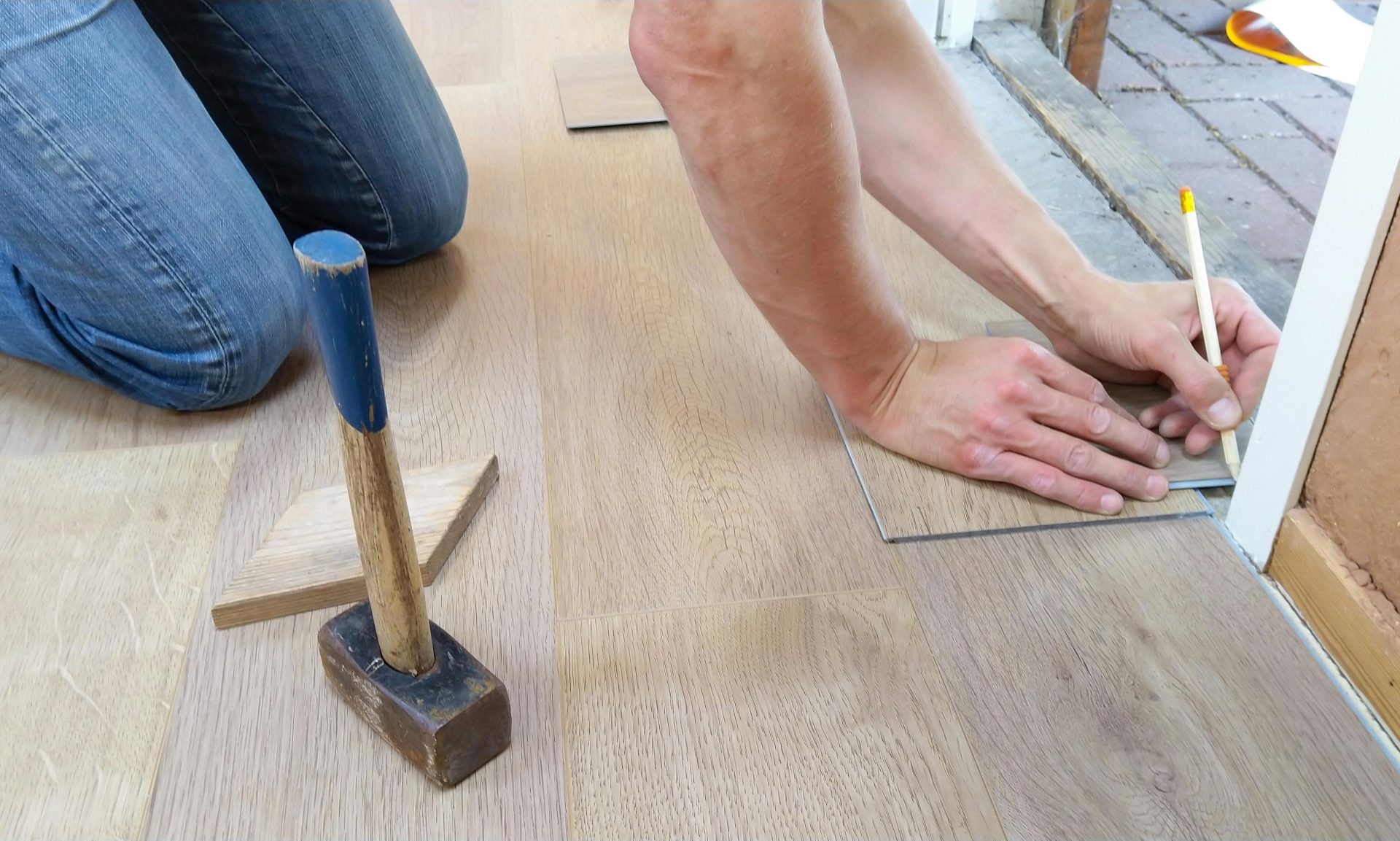 Ein Handwerker vermisst und markiert sorgfältig Holzfußbodenpaneele für eine präzise Verlegung.