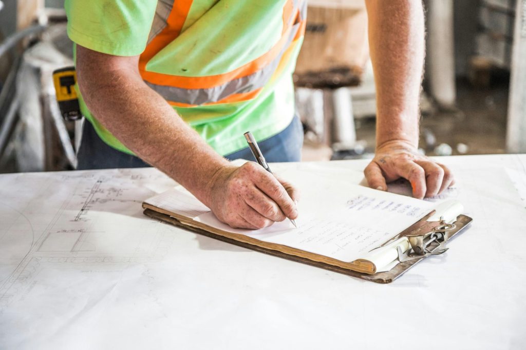Ein Bauarbeiter macht sich auf einer Baustelle Notizen auf einem Klemmbrett und betont dabei Planung und Präzision.