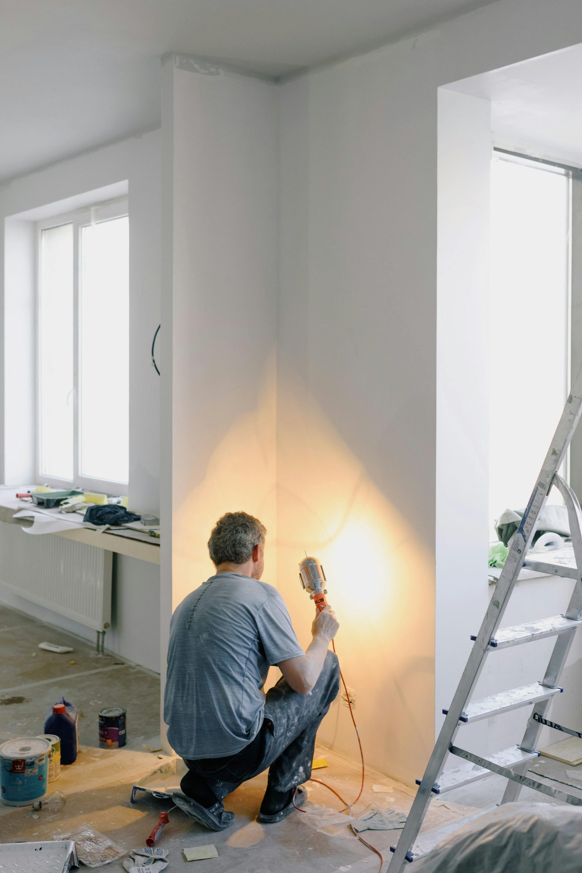 Rückansicht eines anonymen Mannes in schmutziger Kleidung, der mit einer Lampe in der Hand Wände in seinem Haus renoviert.